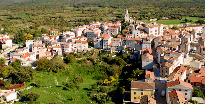 The hilltop village of Bale seen from above, red roofs and the church bell tower surrounded by green fields