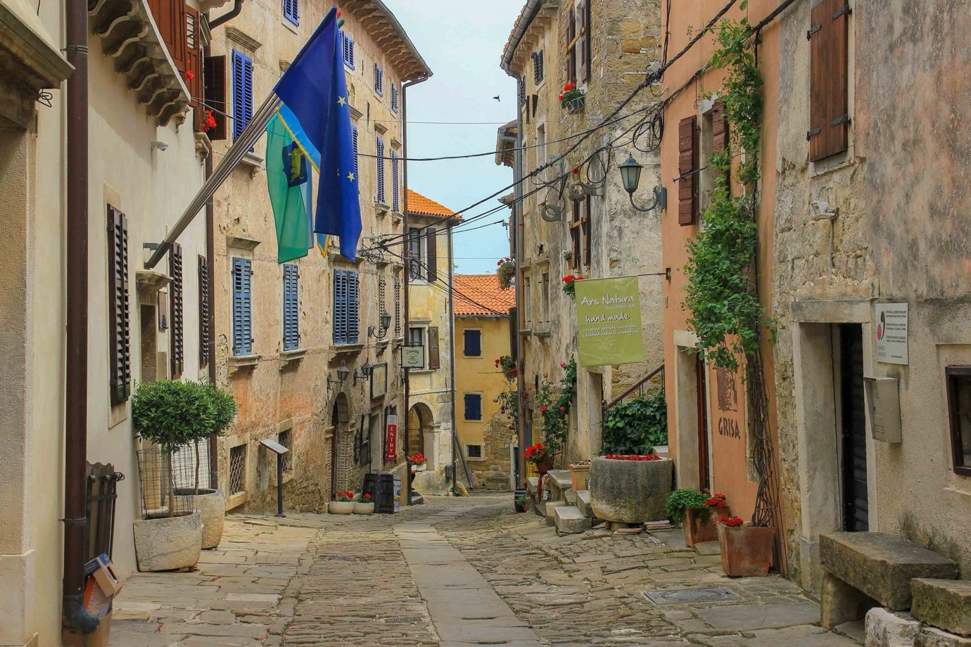 A narrow street of pale stone houses in Grožnjan with potted plants and a flag